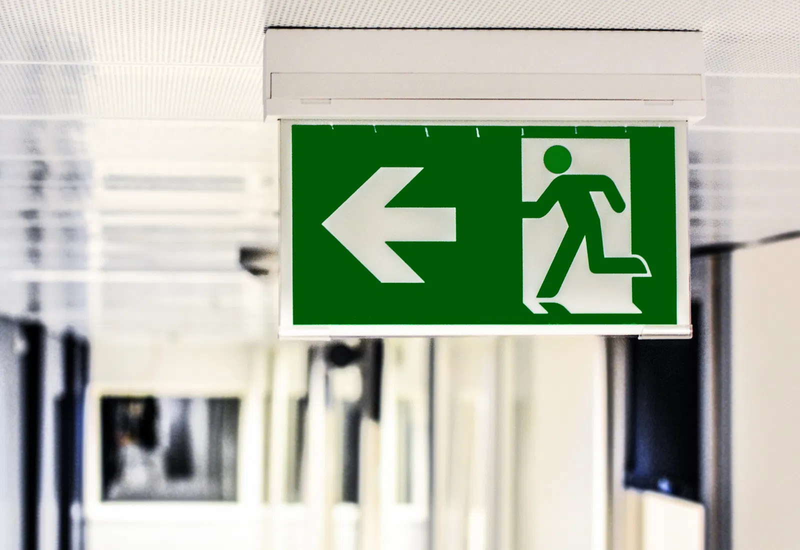 Panneau vert de sortie de secours avec flèche à gauche dans un bâtiment commercial, important pour la sécurité et l'évacuation.