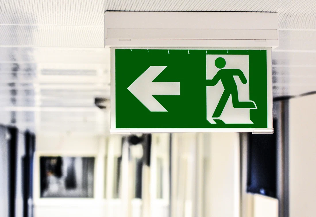 Señal verde de salida de emergencia con flecha a la izquierda en un edificio comercial, importante para la seguridad y evacuación.