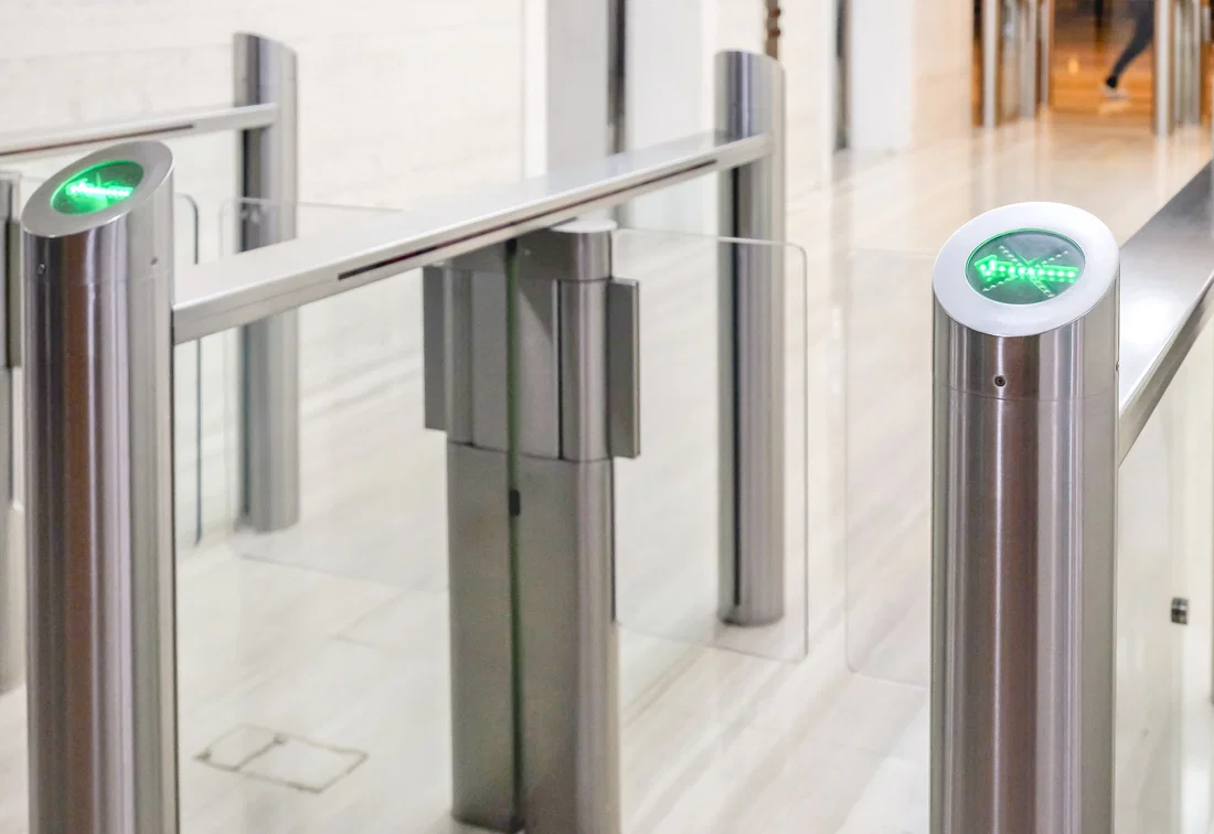 Glass speedgate turnstiles with green access lighting in a modern office lobby.