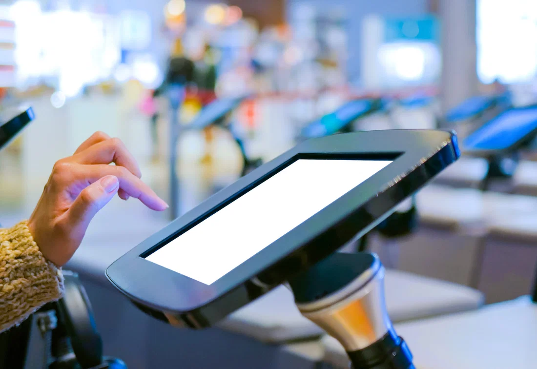 A hand taps on a self-service tablet kiosk to check visitors in at a virtual reception desk.