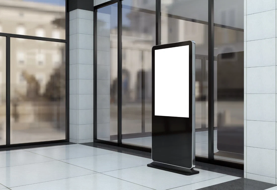 Freestanding digital kiosk in a modern office lobby, used as a virtual welcome screen at the reception desk.