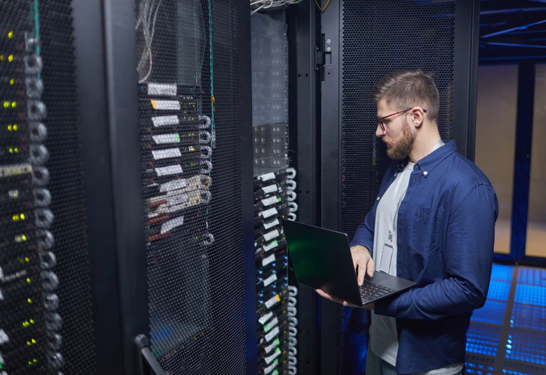 IT employee checking servers with a laptop in a data center.