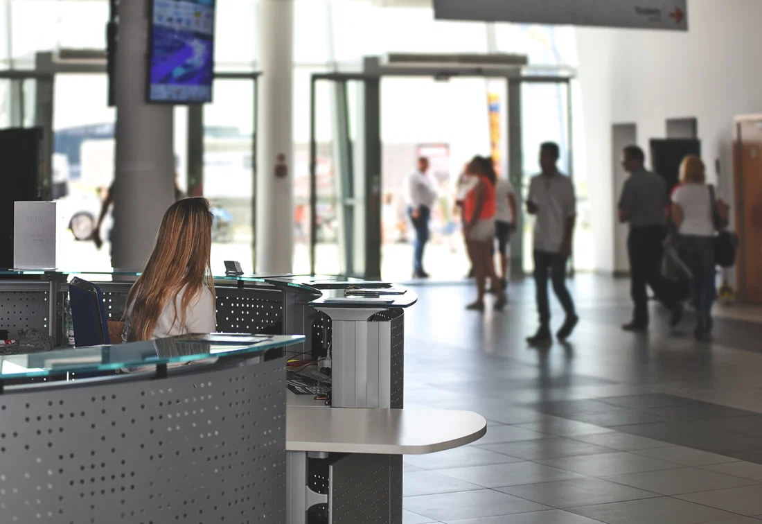 Receptionist al bancone in una hall d'ingresso affollata con visitatori sullo sfondo.