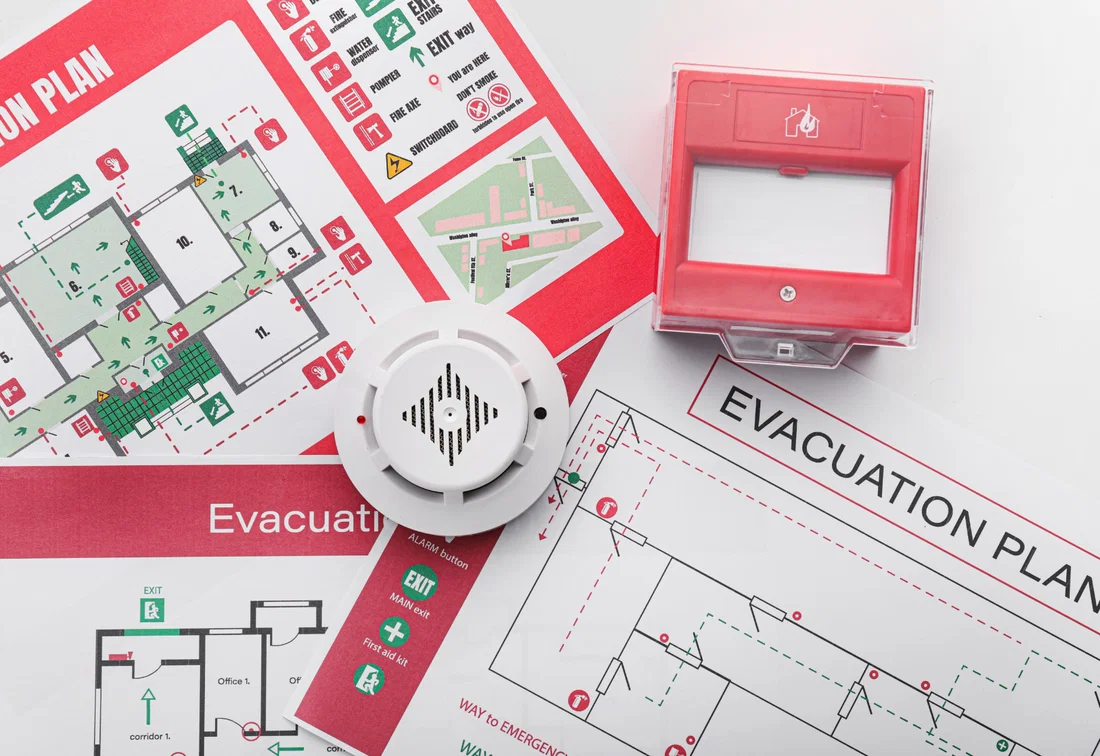 Evacuation plans next to a smoke detector and a manual fire alarm call point in the workplace.